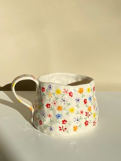 a white vase with colorful flowers on it sitting on a table next to a wall