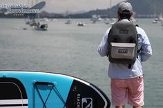 a man with a back pack standing next to a body of water filled with boats