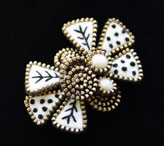 a black and white flower brooch with dots on it's center, sitting on a black surface