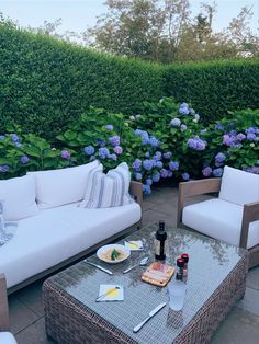 an outdoor patio with wicker furniture and blue hydrangeas in the back ground