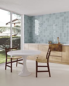 a white table and two chairs in a room with blue tiles on the wall behind it