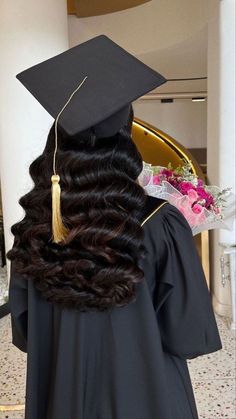 a woman wearing a graduation cap and gown with long curly hair in the middle of her body