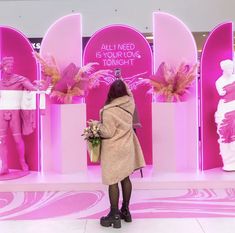 a woman standing in front of a pink display with flowers and statues on it's sides