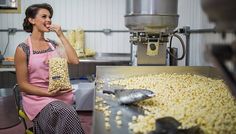 a woman in an apron is eating popcorn from a machine and smiling at the camera