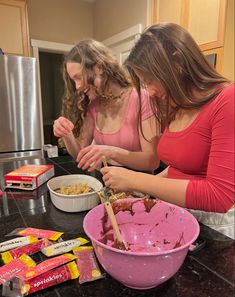 two girls are preparing food in the kitchen with pink bowls and candy bars on the counter