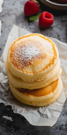 three pancakes stacked on top of each other with powdered sugar and strawberries in the background