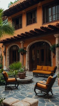 an outdoor seating area with chairs and potted plants in front of a large orange building