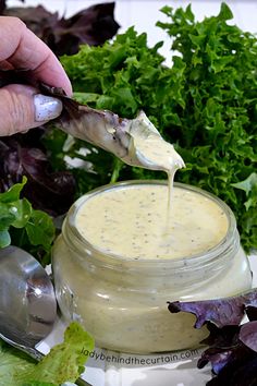 a person dipping something into a jar filled with salad dressing next to lettuce