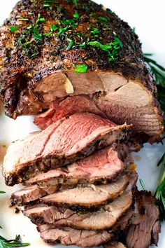 sliced roast beef on a white plate with fresh herbs