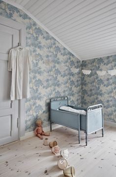 a baby's room with blue floral wallpaper and wooden flooring, including a crib