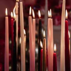 many lit candles are lined up in a row with red and white ones behind them