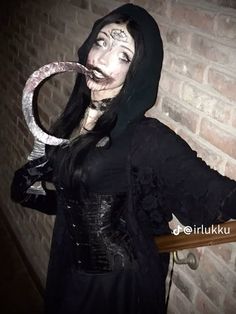 a woman dressed up as a nun holding a snake in her hand and wearing black clothing