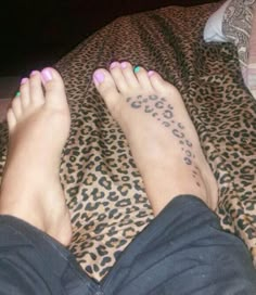 a woman's feet with tattoos on them laying on a leopard print bed spread