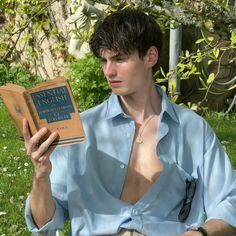 a man sitting in the grass holding an open book with his shirt off and no shirt on