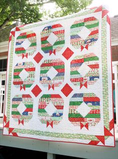 a large quilt is hanging on the side of a building with trees in the background