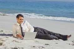 a man laying on the beach with his laptop