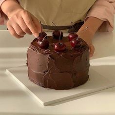 a person cutting into a chocolate cake with cherries on it