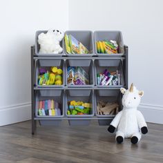 a stuffed animal sitting next to a toy storage unit with bins on the floor