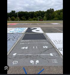 an empty parking lot with arrows painted on the pavement and trees in the background,