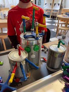 a young boy wearing a red shirt standing in front of tin cans with construction tools on them