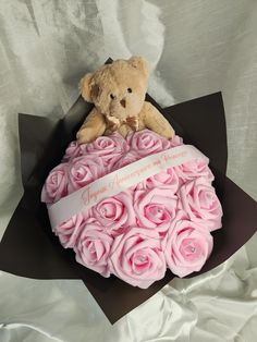 a teddy bear sitting on top of a bouquet of pink roses in a black box