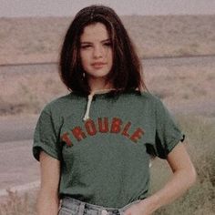 a woman standing in the grass with her hands on her hips wearing a green shirt that says trouble