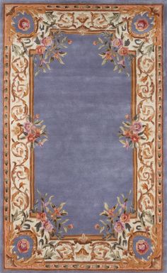 a blue rug with an ornate border and flowers on the bottom, in front of a gray background