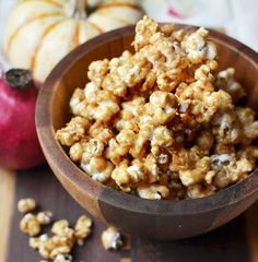 a wooden bowl filled with caramel popcorn next to an apple and other fall decorations