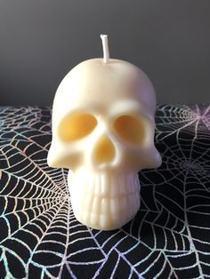 a white skull candle sitting on top of a spider web tablecloth with a black background