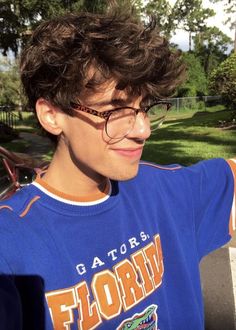 a young man wearing glasses and a florida gators t - shirt in the park