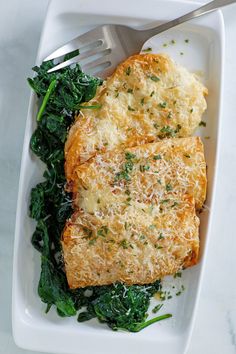 two pieces of bread with cheese and greens on a white plate next to a fork