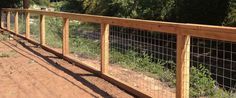 a wooden and wire fence on the side of a dirt road with trees in the background