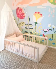 a baby's bed in front of a painted wall with flowers and clouds on it