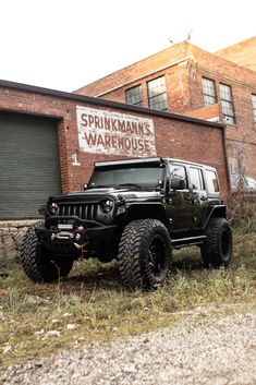 a black jeep parked in front of a brick building with an old sign on it