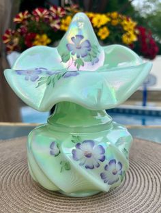 a glass vase with flowers painted on it sitting on a table next to a pool