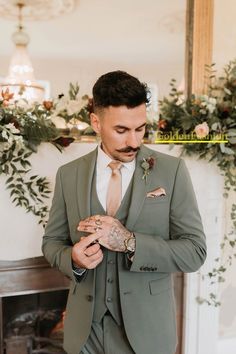 a man wearing a suit and tie standing in front of a fireplace with greenery