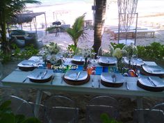 a table set up with plates and silverware at the beach for an outdoor dinner