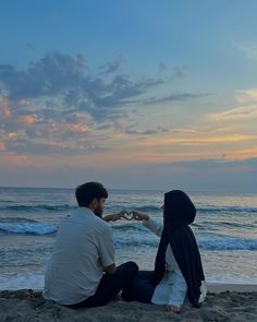 a man and woman sitting on the beach holding hands