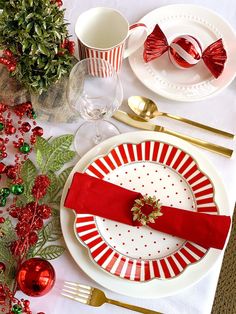 the table is set for christmas dinner with red and white plates, silverware, gold utensils and candy canes