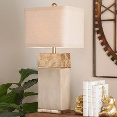 a table lamp sitting on top of a wooden desk next to a book and gold figurines