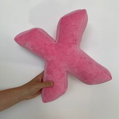 a person holding a pink stuffed toy shaped like an x on a white table top