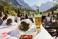 there is a large sandwich and a drink on the table at an outdoor restaurant with mountains in the background