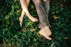 a person laying on the ground with their feet up in some grass and bushes next to them