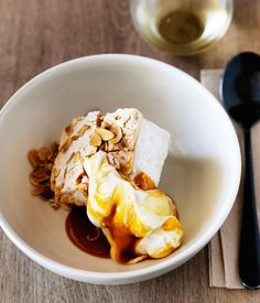 a white bowl filled with food next to a glass of wine on top of a wooden table