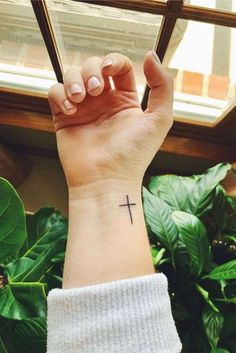 a woman's wrist with a small cross tattoo on the middle of her arm