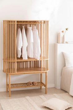 a wooden shelf with clothes hanging on it in a white room next to a bed