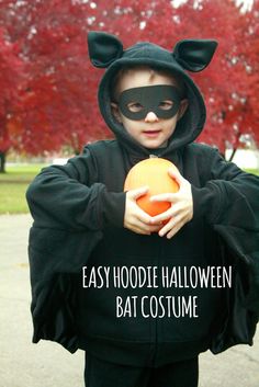 a young boy dressed up as a cat holding an orange in his hands with the words easy hoodie halloween bat costume