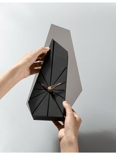 two hands holding an origami clock in front of a gray background with gold hands