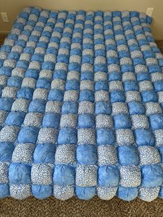 a bed made out of blue and white pillows on carpeted floor next to wall