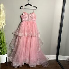 a pink dress hanging on a hanger next to a potted plant and mirror